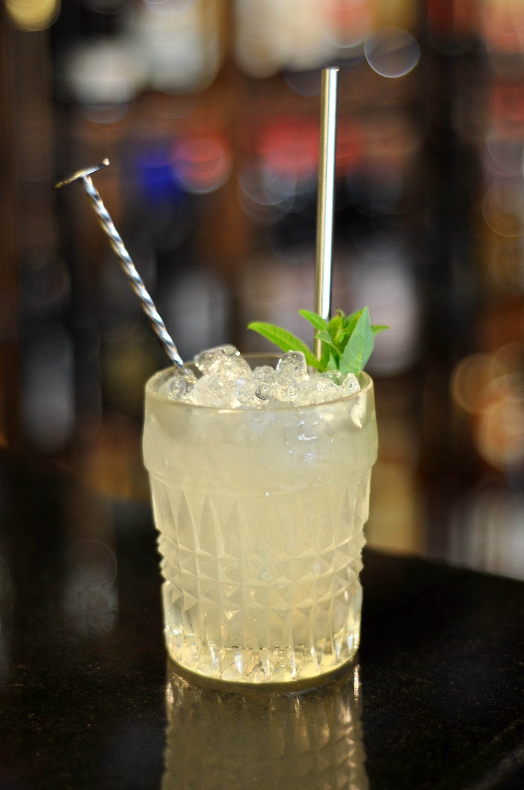 Cocktail dans un verre lehmannde de couleur citronnée accompagné d’une feuille de menthe